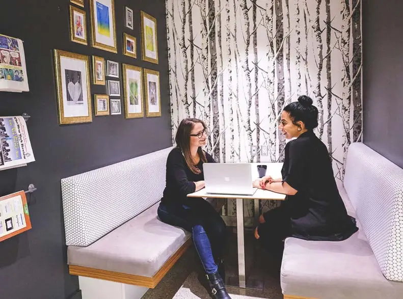 Two Sage Recruiting team members having a conversation over a laptop at a cafe-style table